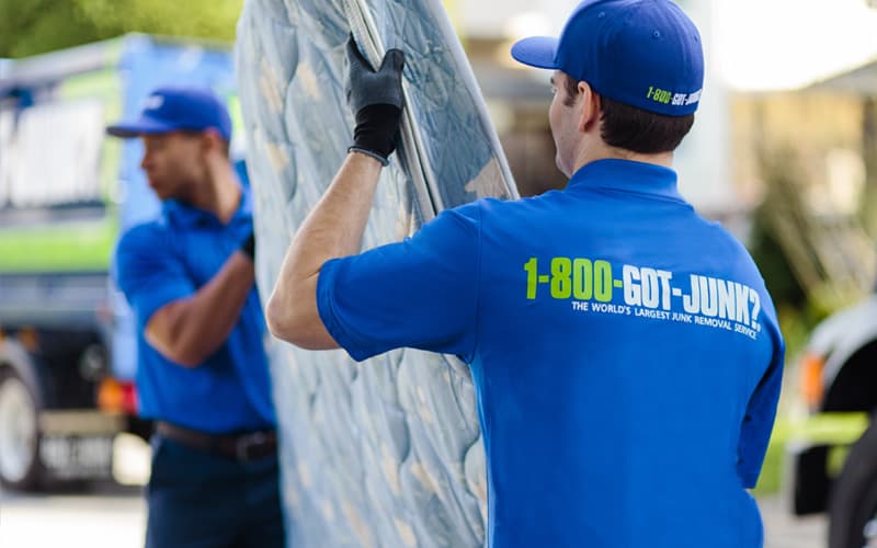 Two 1-800-GOT-JUNK? team members carrying a mattress for recycling Two 1-800-GOT-JUNK? team members carrying a mattress for recycling